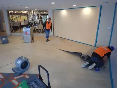 Crew removing wet flooring in a commercial space with an air mover running