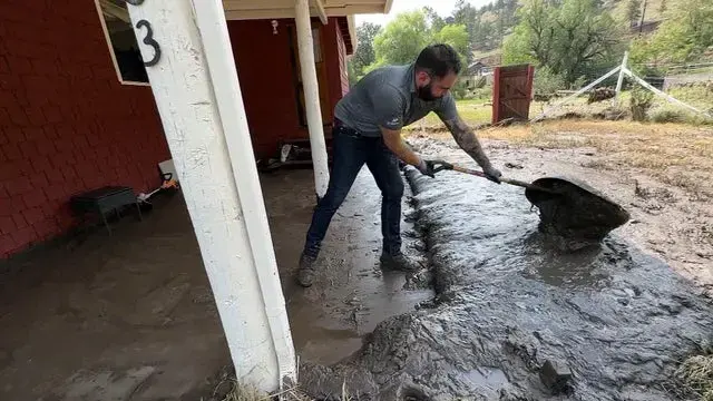 Man shoveling storm mud and runoff from under a carport after heavy rain